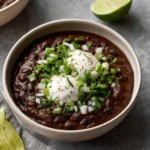 A bowl of Cuban Black Bean Soup garnished with fresh herbs and spices