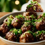 Plate of saucy Asian meatballs garnished with herbs and served with rice
