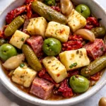 Marinated cheese appetizer with salami and pickles on a platter.