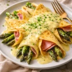 Ham and asparagus crepes served on a plate, garnished with herbs.