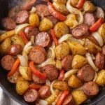 A plate of kielbasa and potatoes garnished with fresh herbs.
