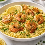 Plate of Lemon Garlic Shrimp Orzo garnished with herbs and lemon slices.
